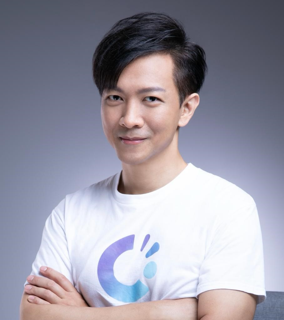 A person with black hair and a white shirt with blue and purple logo
                Description automatically generated